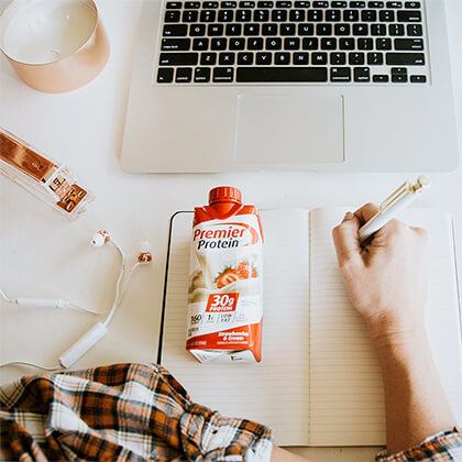 Premier Protein shake on table next to open laptop